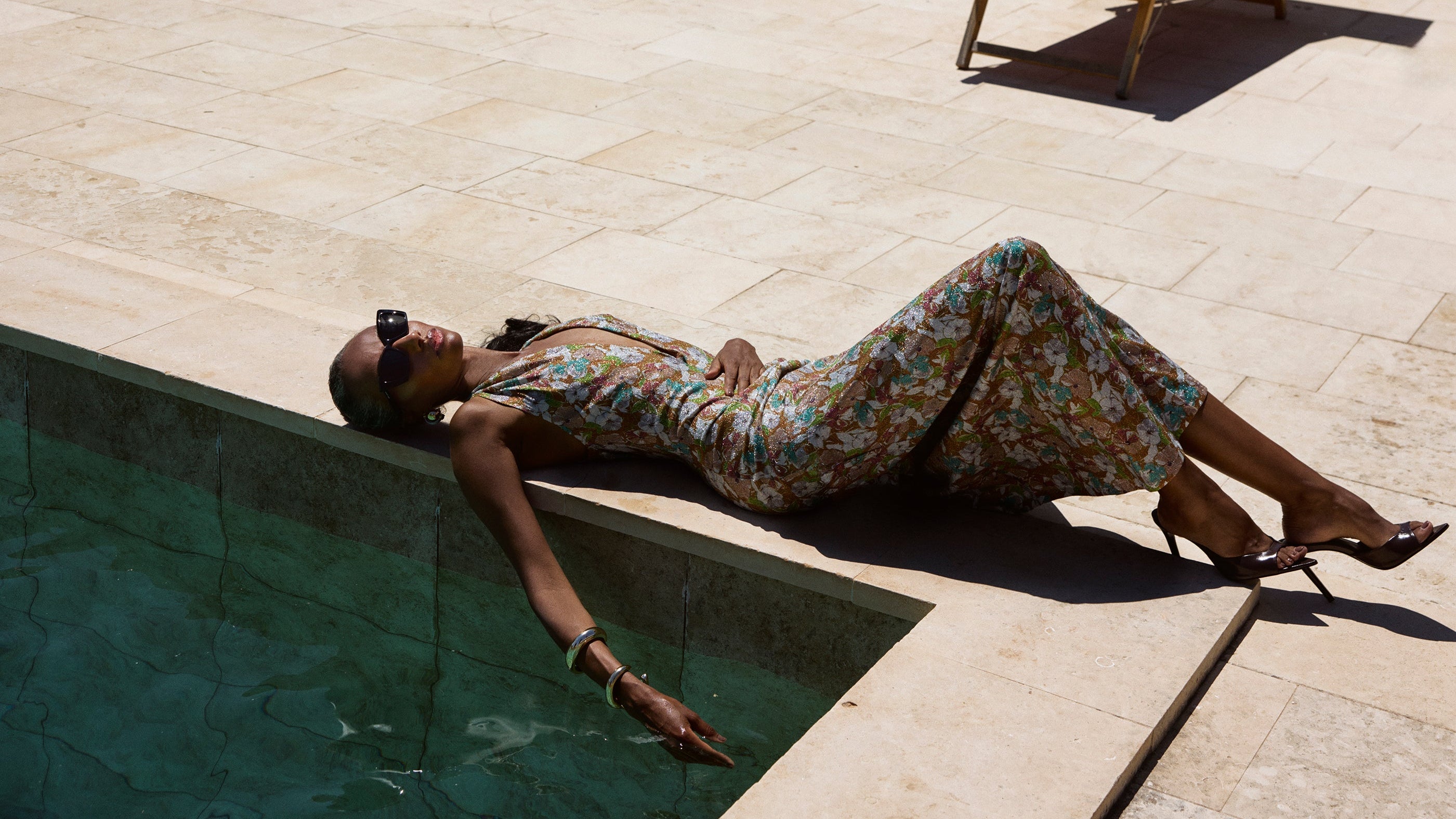 Woman lying by a pool with a lounge chair and potted plants in the background